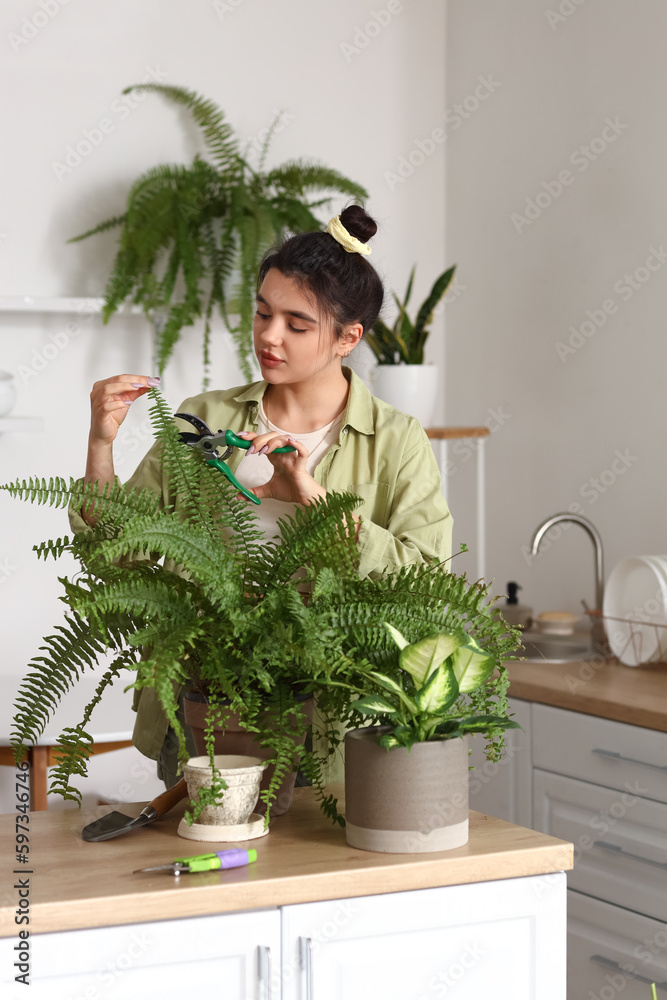 Young woman cutting plant branch in kitchen Young woman cutting plant branch in kitchen