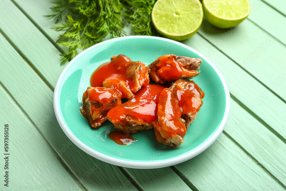 Plate with canned fish in tomato sauce, lime and dill on green wooden table Plate with canned fish in tomato sauce, lime and dill on green wooden table