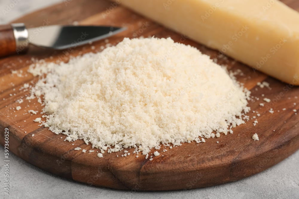 Wooden board with tasty grated Parmesan cheese on grunge background, closeup Wooden board with tasty grated Parmesan cheese on grunge background, closeup