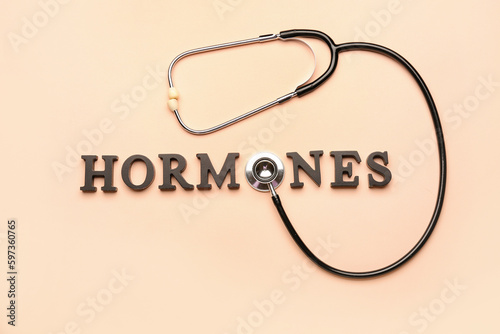 Word HORMONES with stethoscope on beige background