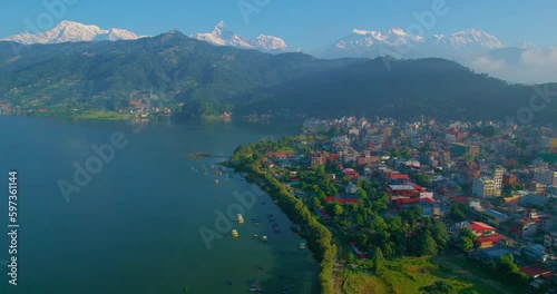 Drone captures a breathtaking view of Pokhara city as it glides left, revealing the pristine Phewa Lake, bustling Lakeside, and the majestic Macchapuchhre and Annapurna mountain range in the distance. photo