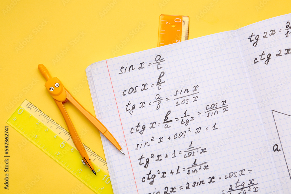 Copybook with maths formulas and stationery on yellow background Copybook with maths formulas and stationery on yellow background