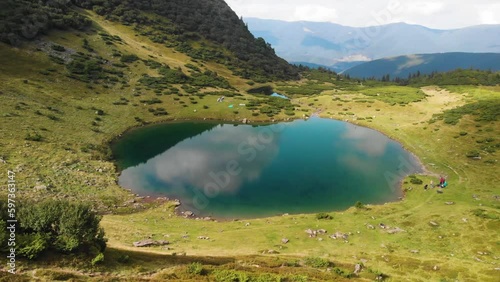 Hikers camping near the lake in the mountains in the summer aerial footage. Nesamovyte lake, Carpathians, Ukraine, Lake Vorozheska