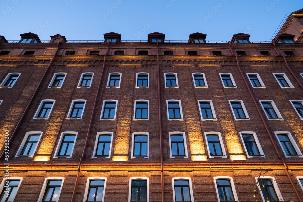 Fototapeta premium The wall of an old brick house in the evening with lighting.