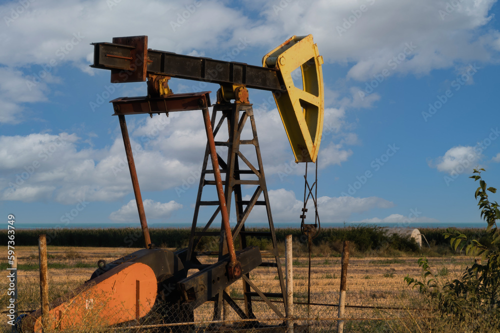 A small oil pump, an energy industrial oil machine, in the agricultural field in Bulgaria. In the background is the Black Sea A small oil pump, an energy industrial oil machine, in the agricultural field in Bulgaria. In the background is the Black Sea
