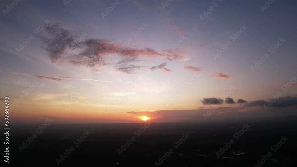 Sunset sky at central Bali, aerial low angle shot, camera fly high. Small tattered cloud in dark blue colored with red from setting sun. Land in shadow, bright spot of sun shine low over horizon Sunset sky at central Bali, aerial low angle shot, camera fly high. Small tattered cloud in dark blue colored with red from setting sun. Land in shadow, bright spot of sun shine low over horizon