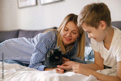 Portrait of family, mother and son lying on bed at the weekend together at home and petting cat