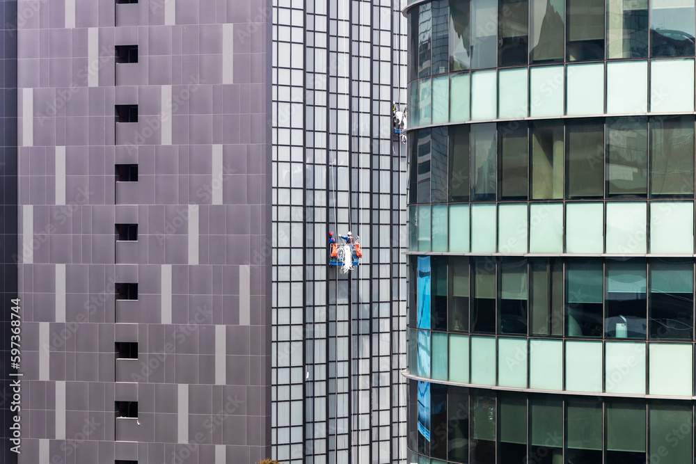 Group of worker cleaning glass windows on high skyscraper building.Workers with safety helmets and rope construct maintenance or paint the building.Window cleaner working on facade of building.