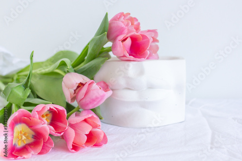 Pink tulips bouquet and plaster statue of lips lying on white wrinkled blanket background copy space