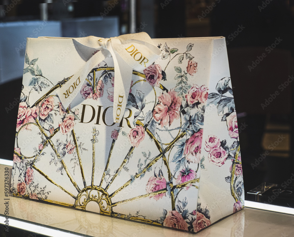 Foto Stock Elegant gift package packaged in a floral print bag closed with  white ribbon with gold Dior logo.Milan - Italy,22 April 2023 | Adobe Stock