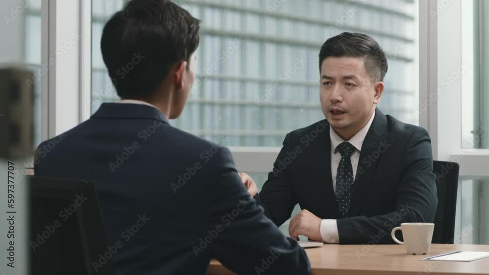 asian manager sitting at desk talking to colleague in office asian manager sitting at desk talking to colleague in office