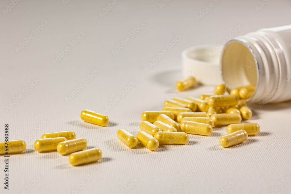 Yellow pills for oral use on a white background. Medications in the form of tablets in a white plastic jar. Yellow pills for oral use on a white background. Medications in the form of tablets in a white plastic jar.