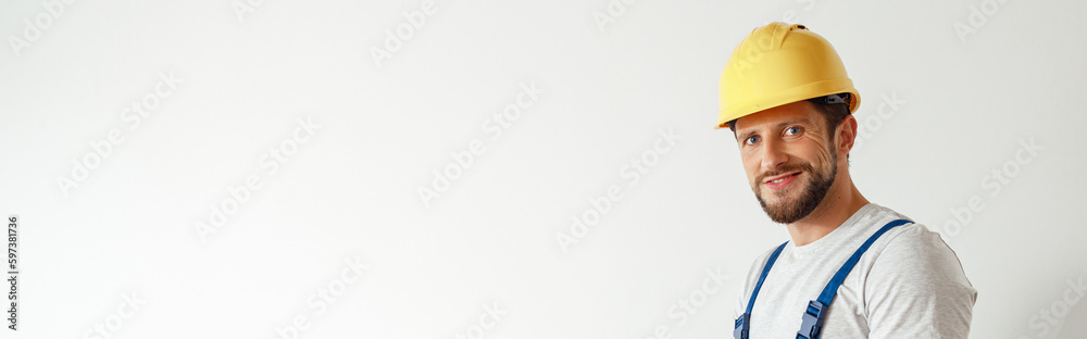 Smiling handyman worker, builder in uniform and hard hat looking at camera, making notes on a clipboard while standing indoors Smiling handyman worker, builder in uniform and hard hat looking at camera, making notes on a clipboard while standing indoors