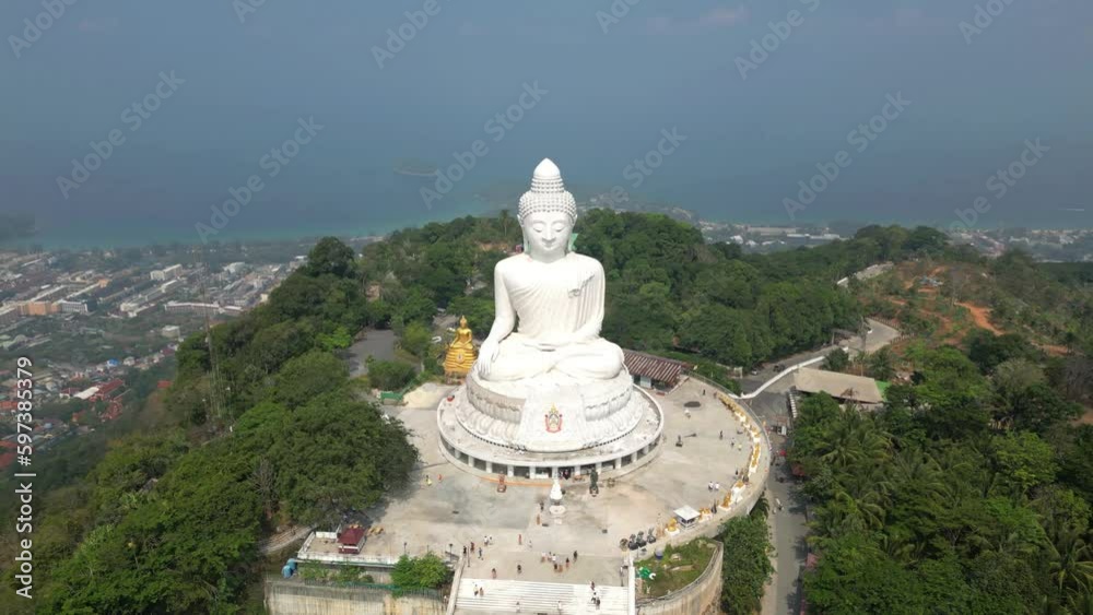 Wide, high altitude aerial view of Big Buddha in Phuket, Thailand from drone orbiting. Ocean and city in background. People visit huge Buddha templet monument for religious worship tourist attraction.