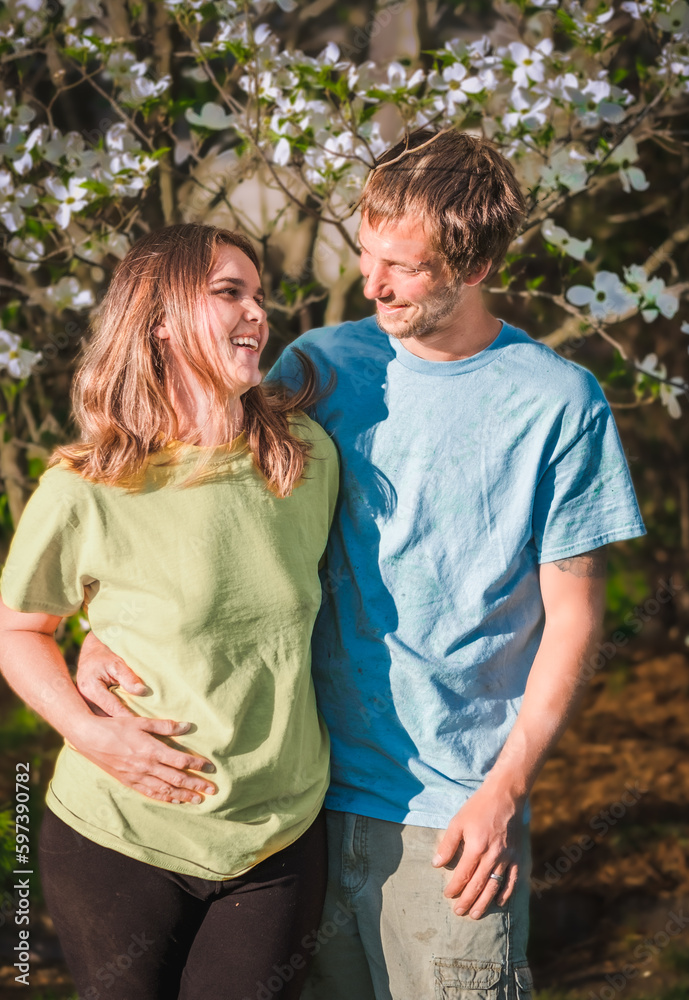 Casually dressed young couple smiling at each other; blooming tree in background Casually dressed young couple smiling at each other; blooming tree in background