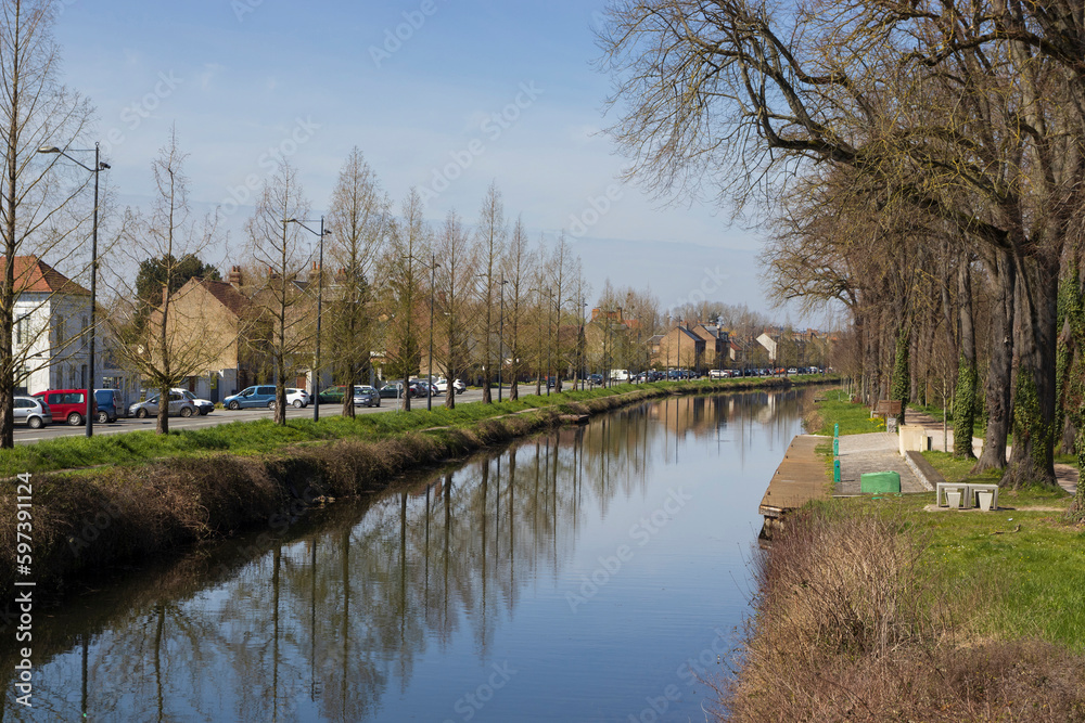 Early spring view of the Canal de Transit in Abbeville, in the Somme Department of Northern France. Tree-lined tranquil waterway with clear blue sky, and sunshine.