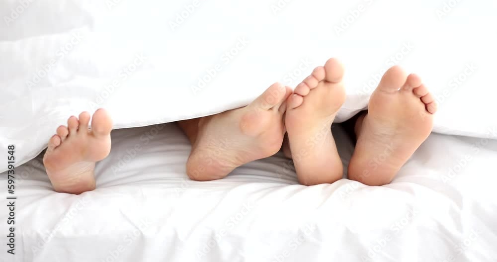 Barefoot man touches foot of woman lying in bed in morning. Bare feet of married couple stick out of white blanket in bedroom slow motion Barefoot man touches foot of woman lying in bed in morning. Bare feet of married couple stick out of white blanket in bedroom slow motion