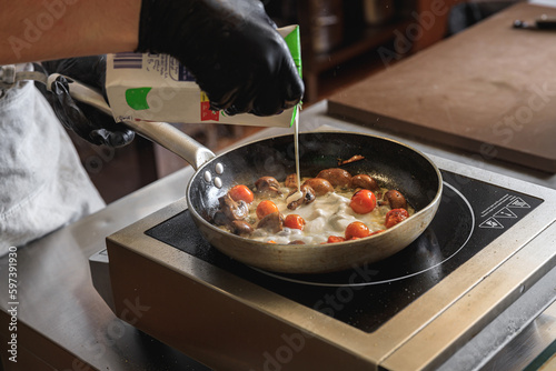 Canvas-taulu The professional chef in uniform adding cream into frying pan with dish in resta
