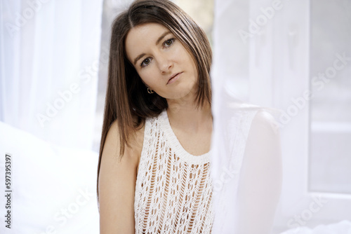 Portrait of a beautiful woman wearing white top, knitted or crocheted, sitting relaxed in bed