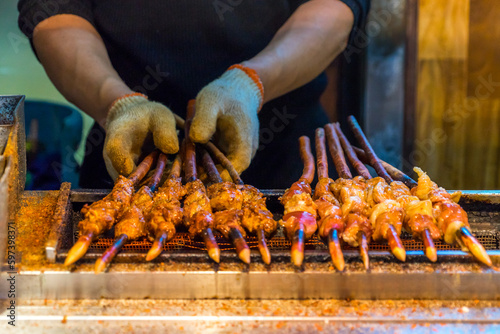 Man hands cooking grilled meat with Mala chilli on a stick at Muslim street food, China. Chinese food style.