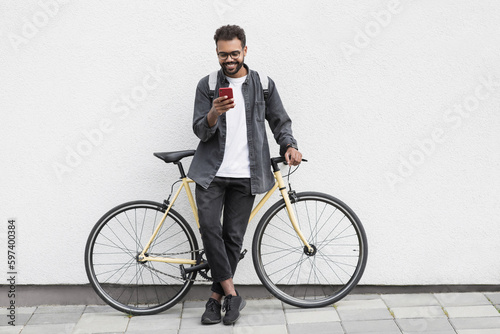 Fototapeta Naklejka Na Ścianę i Meble -  Young handsome man with bicycle over white wall background in a city, cheerful student men with mobile phone smiling outdoor, Modern lifestyle, travel, casual business, connection concept