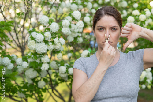 A woman suffers from a clothespin on her nose and shows a thumbs down on a walk in a flowering park. Allergy.