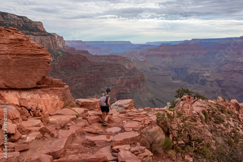 Front view of woman with backpack hiking along South kaibab trail with panoramic aerial overlook of South Rim of Grand Canyon National Park, Arizona, USA, America. Amazing vista in the Southwest
