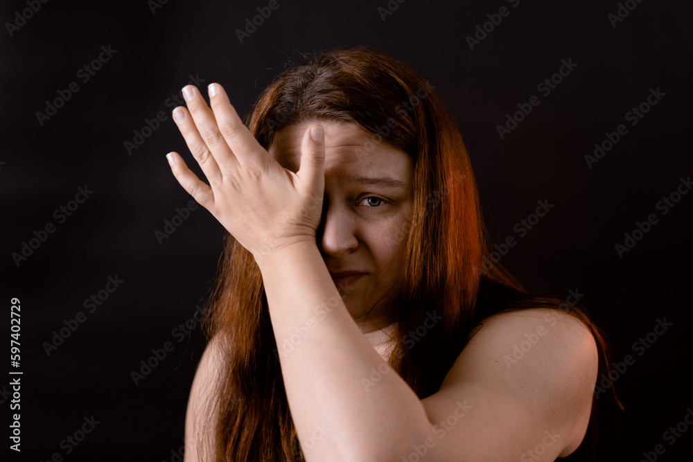Obraz premium Crying sad young woman wiping eyes with hand. Female portrait isolated on black. Upset girl suffering from pain. Feelings, life difficulties. Human emotions, facial expression concept.