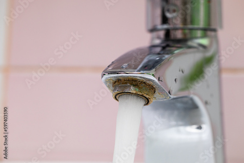 Fényképezés Flowing tap water running from corrosive steel spigot, flow on backdrop of pink tiled