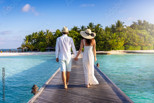 Fototapeta A elegant couple walks down a wooden pier over turquoise sea in the Maldives isl