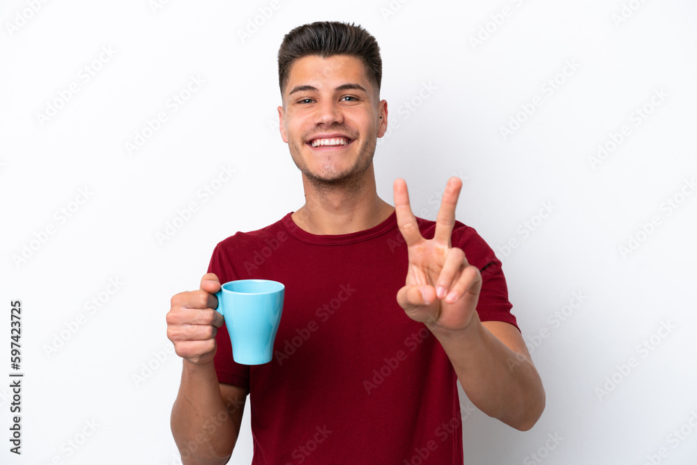 Young caucasian man holding cup of coffee isolated on white background smiling and showing victory sign Young caucasian man holding cup of coffee isolated on white background smiling and showing victory sign