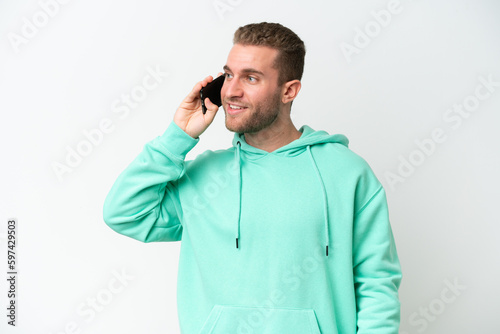 Young handsome caucasian man isolated on white background keeping a conversation with the mobile phone © luismolinero