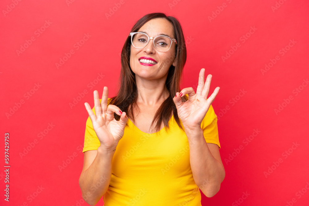 Middle-aged caucasian woman isolated on red background showing ok sign with two hands Middle-aged caucasian woman isolated on red background showing ok sign with two hands