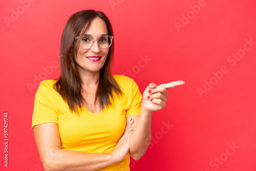 Middle-aged caucasian woman isolated on red background pointing finger to the side