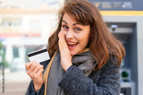 Brunette woman holding a credit card at outdoors whispering something
