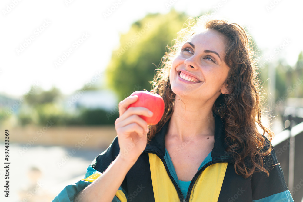 Young sport woman with an apple at outdoors looking up while smiling Young sport woman with an apple at outdoors looking up while smiling