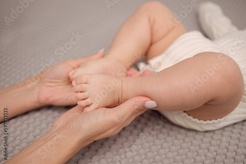 A young woman holding a baby's hand and little leg. A little baby and a mother, tenderness, care, nursing, health.