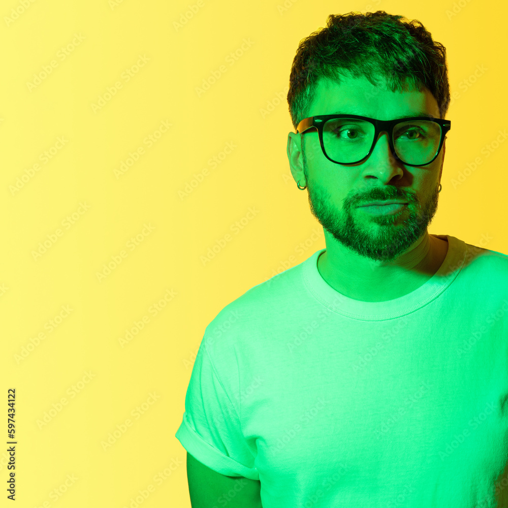 Creative portrait of a bearded middle-aged man with black framed glasses. Depressed man with mental problems sadly looking away. Colored green light on yellow background. Concept midlife crisis