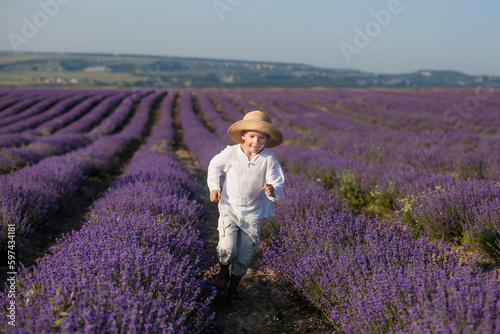 A 6 or 7-year-old boy in a straw hat and light clothing in a lavender field, in the summer sun