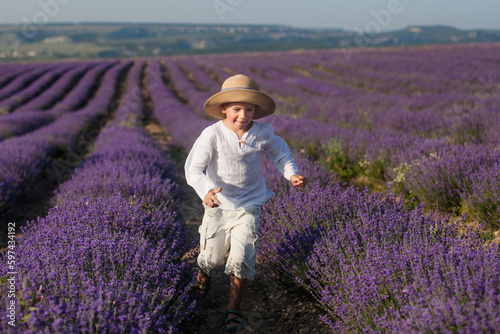 A 6 or 7-year-old boy in a straw hat and light clothing in a lavender field, in the summer sun