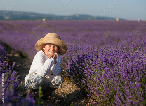 A 6 or 7-year-old boy in a straw hat and light clothing in a lavender field, in the summer sun © Ksenia