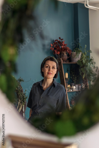 Portrait of a young attractive female florist in the reflection of a mirror decorated with stabilized moss and plants.Biophilia design concept.Selective focus. photo