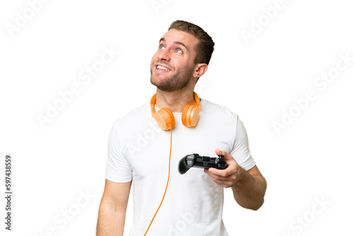 Young handsome man playing with a video game controller isolated on green chroma background looking up while smiling