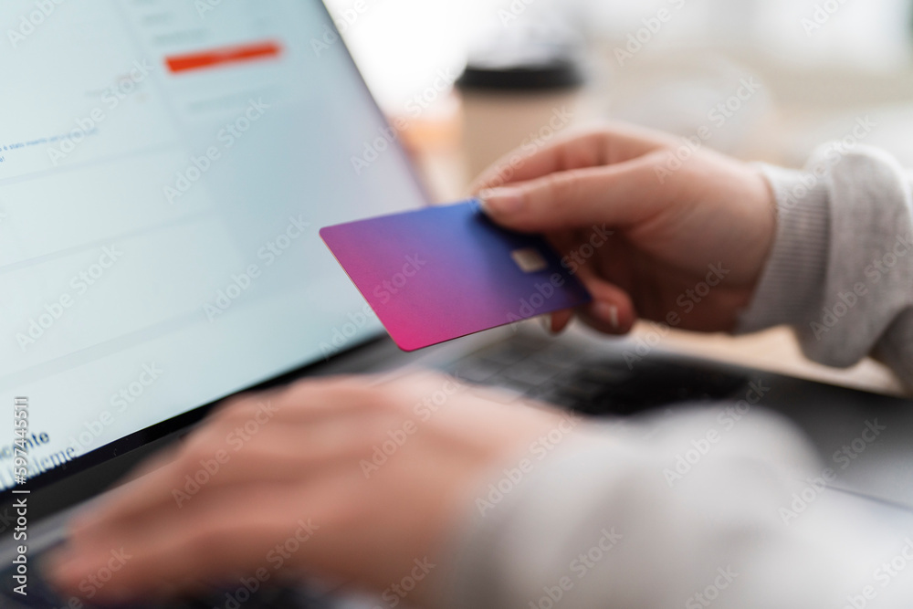 Crop anonymous female hand holding a credit card, doing online shopping on computer
