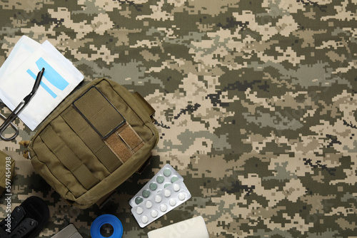 Flat lay composition with military first aid kit on camouflage fabric. Space for text photo