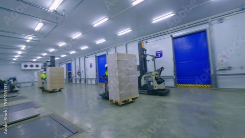 Forklifts unloading cargo from container at distribution warehouse. FPV drone