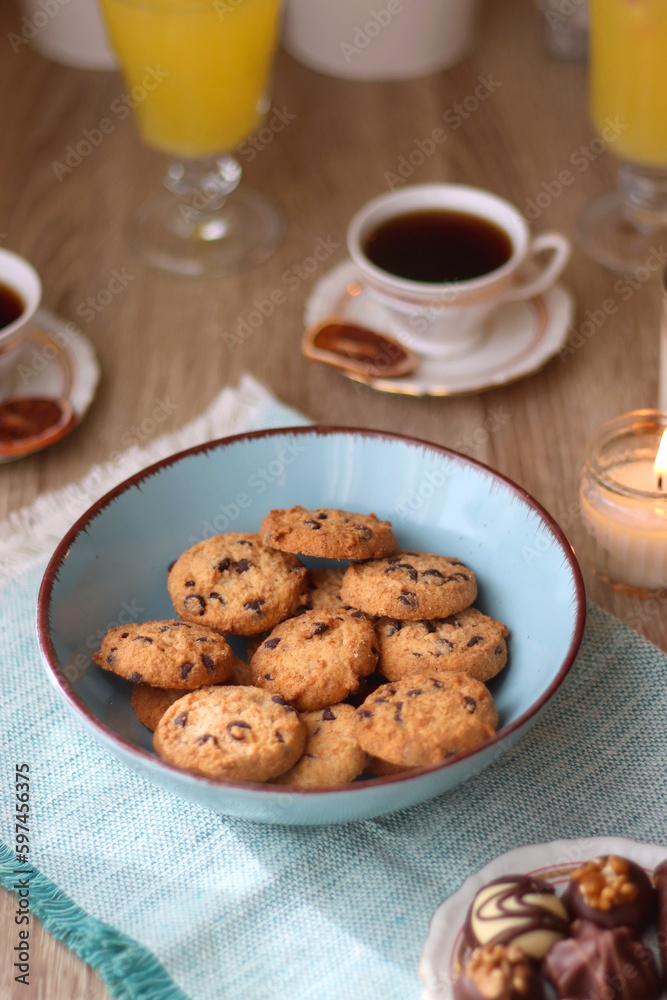 Plate of chocolate pralines, bowl of cookies, cups of tea, glasses of juice and lit candles on the table. Selective focus. Plate of chocolate pralines, bowl of cookies, cups of tea, glasses of juice and lit candles on the table. Selective focus.