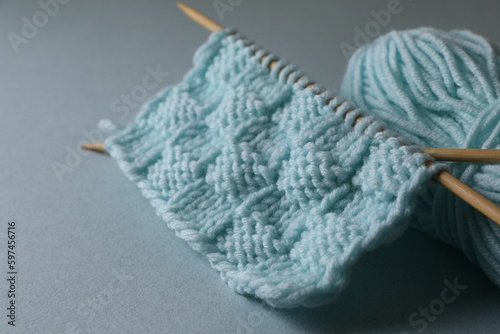 Soft turquoise knitting and needles on light blue background, closeup