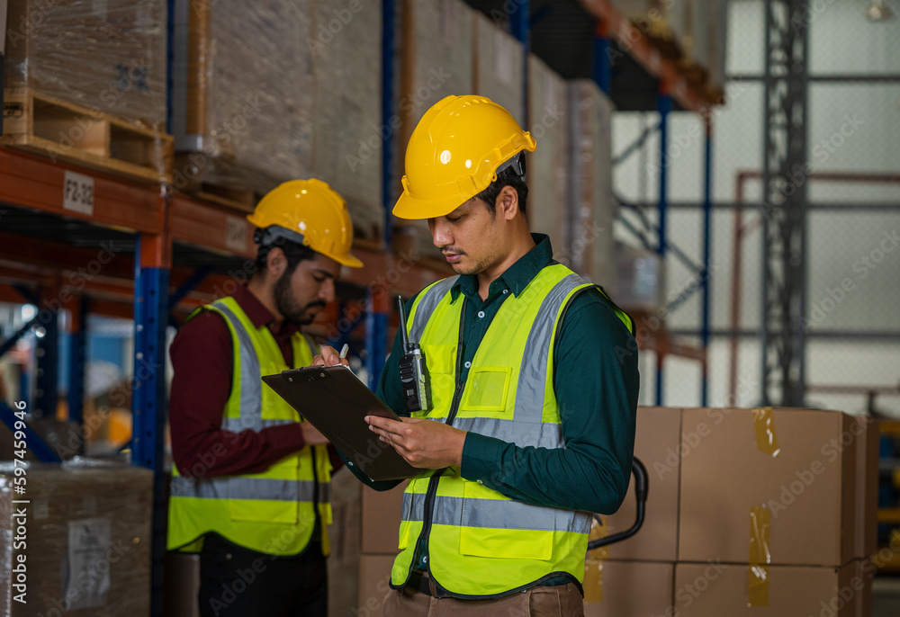 Warehouse employees using digital tablet computer for checking stock in a large distribution warehouse.