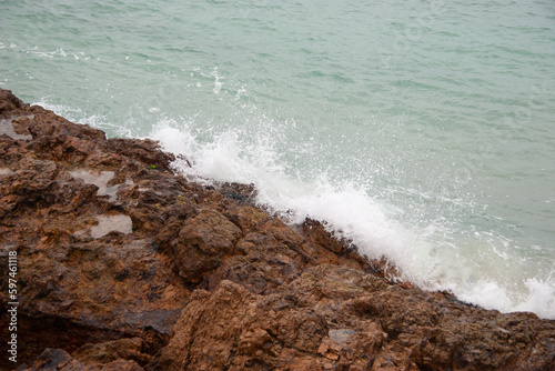 Top view of ocean water splashing against wall of rugged brown rocks photo